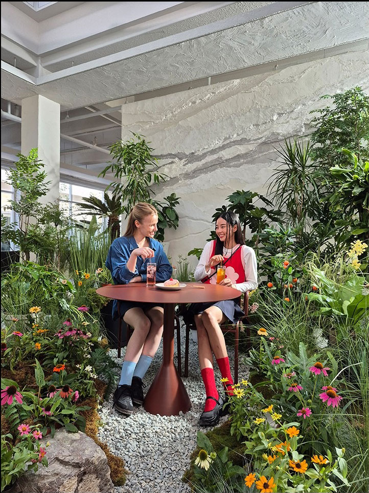 A photo of two people sitting together at a table surrounded by vibrant indoor plants and flowers. Text reads Captured by Galaxy S24 FE #withGalaxy.